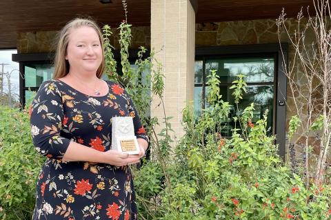 Elizabeth Marzec with her new trophy, in front of the center’s pollinator garden that she helped develop. Photo by Niko Demetriou